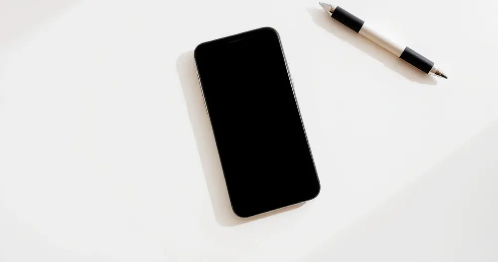 Celular apoiado com a tela voltada para baixo sobre mesa clara ao lado de caderno e caneta