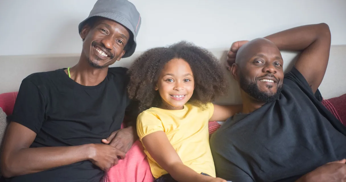 Família sorrindo no sofá enquanto assiste à televisão, ilustrando a TV da família